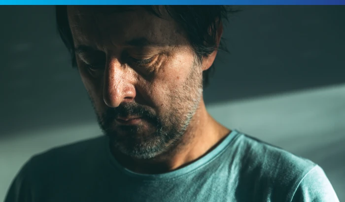 Adult male in soft natural lighting with a dark green background.