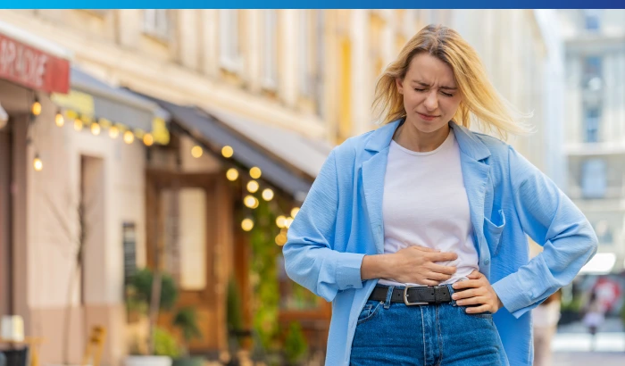 Woman standing outdoors holding her stomach, representing abdominal discomfort.